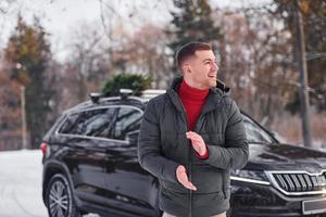 homem com pequeno abeto verde está ao ar livre perto de seu carro. concepção de férias foto