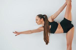 de pé contra um fundo branco. jovem em roupas esportivas fazendo ginástica dentro de casa foto