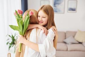 abraçando um ao outro. jovem mãe com sua filha está em casa durante o dia foto