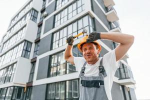 de pé perto de edifícios modernos. jovem trabalhando de uniforme na construção durante o dia foto