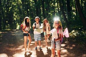 posando para a câmera. crianças passeando na floresta com equipamentos de viagem foto