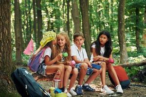 sentado no acampamento. crianças passeando na floresta com equipamentos de viagem foto