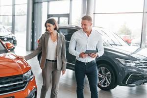 carro de cor laranja. homem com roupa formal ajudando cliente na escolha do automóvel foto