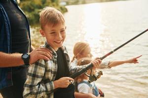 aprendendo a pescar. pai e mãe com filho e filha juntos ao ar livre no verão foto