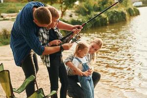 aprendendo a pescar. pai e mãe com filho e filha juntos ao ar livre no verão foto