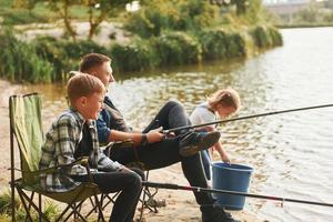 sentados juntos. pai com filho e filha na pesca ao ar livre no verão foto