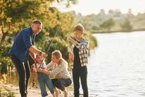 no verão. pai e mãe com filho e filha pescando juntos ao ar livre foto