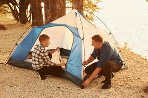 pai e filho instalando barraca ao ar livre perto do lago foto