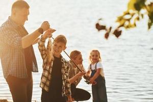 iluminada pela luz solar. pai e mãe com filho e filha pescando juntos ao ar livre no verão foto