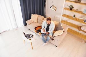 fazendo uma música. homem em roupas casuais e com violão está dentro de casa foto