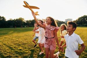 brincando com avião de brinquedo. grupo de crianças felizes está ao ar livre no campo esportivo durante o dia foto