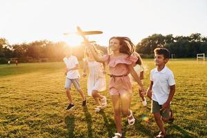 brincando com avião de brinquedo. grupo de crianças felizes está ao ar livre no campo esportivo durante o dia foto