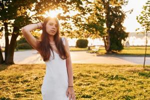 em vestido branco. mulher em pé no parque outono. lindo sol foto