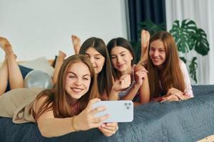 deitada na cama com smartphone. grupo de mulheres felizes que está em uma despedida de solteira foto