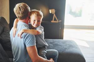 menino abraçando seu pai. pai e filho está dentro de casa juntos foto