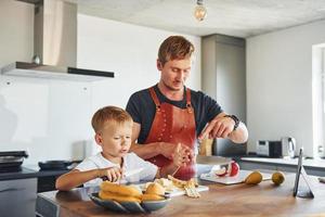 na cozinha com comida. pai e filho está dentro de casa juntos foto