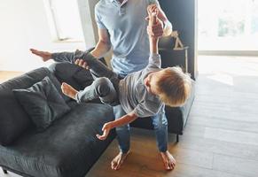 homem segurando o menino e se divertindo. pai e filho está dentro de casa juntos foto