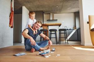 sentado no chão e brincando com brinquedos. pai e filho está dentro de casa juntos foto