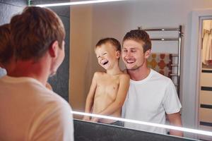 olhando no espelho do banheiro. pai e filho está dentro de casa juntos foto