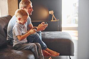 Jogando vídeo game. pai e filho está dentro de casa juntos foto