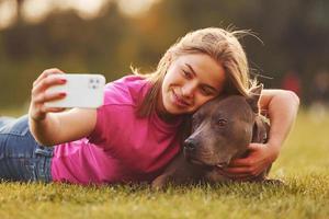 fazendo selfie. mulher em roupas casuais está com pit bull ao ar livre foto