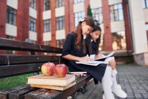 maçãs está no livro. duas alunas estão do lado de fora juntas perto do prédio da escola foto