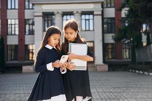 segurando livros. duas alunas estão do lado de fora juntas perto do prédio da escola foto