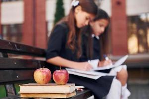 livros e maçãs. duas alunas estão do lado de fora juntas perto do prédio da escola foto