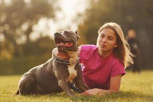 deitado no chão. mulher em roupas casuais está com pit bull ao ar livre foto