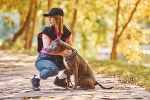 se divertindo. mulher em roupas casuais está com pit bull ao ar livre foto