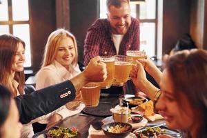 se divertindo. grupo de jovens amigos sentados juntos no bar com cerveja foto