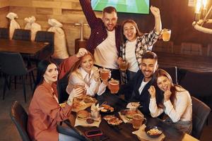 dentro do bar. grupo de jovens amigos sentados juntos com cerveja foto