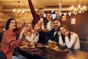 fãs de futebol. grupo de jovens amigos sentados juntos no bar com cerveja foto