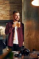 homem com copo de cerveja em pé no bar e sorrindo foto