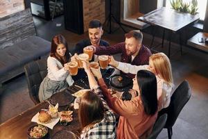 comida deliciosa. grupo de jovens amigos sentados juntos no bar com cerveja foto