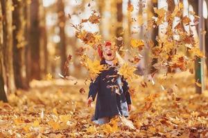 jogando folhas para o ar. linda garotinha positiva divirta-se no parque outono foto