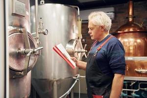 homem sênior está parado no depósito com equipamento para cerveja foto