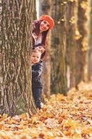 se escondendo atrás de uma árvore. mãe com seu filho e filha está se divertindo no parque outono foto