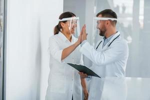 em máscaras de proteção. dois médicos de jaleco branco estão na clínica trabalhando juntos foto