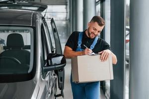 caixa de papel. entregador de uniforme está dentro de casa com carro e com pedido foto