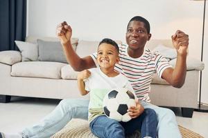 com bola de futebol. pai afro-americano com seu filho em casa foto