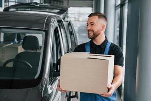 caixa de papel. entregador de uniforme está dentro de casa com carro e com pedido foto