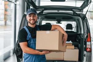 segurando a caixa. entregador de uniforme está dentro de casa com carro e com pedido foto