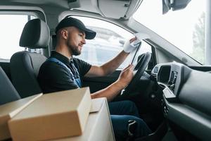 com veículo. entregador de uniforme está dentro de casa com carro e com pedido foto