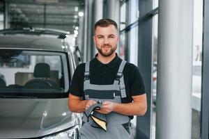 ferramentas nas mãos. homem de uniforme está trabalhando no autosalon durante o dia foto