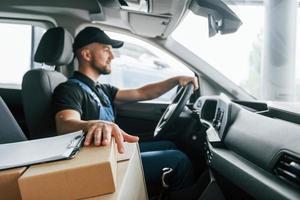 veículo moderno. entregador de uniforme está dentro de casa com carro e com pedido foto