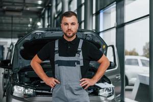 de pé contra o carro. homem de uniforme está trabalhando no autosalon durante o dia foto