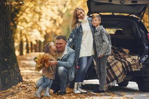 perto de carro com porta-malas aberto. família feliz está no parque no outono juntos foto