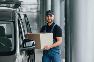 em roupas de cor azul. entregador de uniforme está dentro de casa com carro e com pedido foto