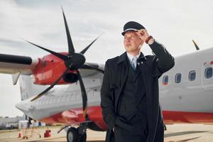 olhando para longe. piloto em uniforme preto formal está ao ar livre perto de avião foto